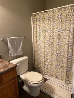 A bathroom with a toilet, a towel hanging on the wall, and a patterned shower curtain. - Cozy Broken Arrow Home -- Special Pricing for 30+ day stays! (Broken Arrow)