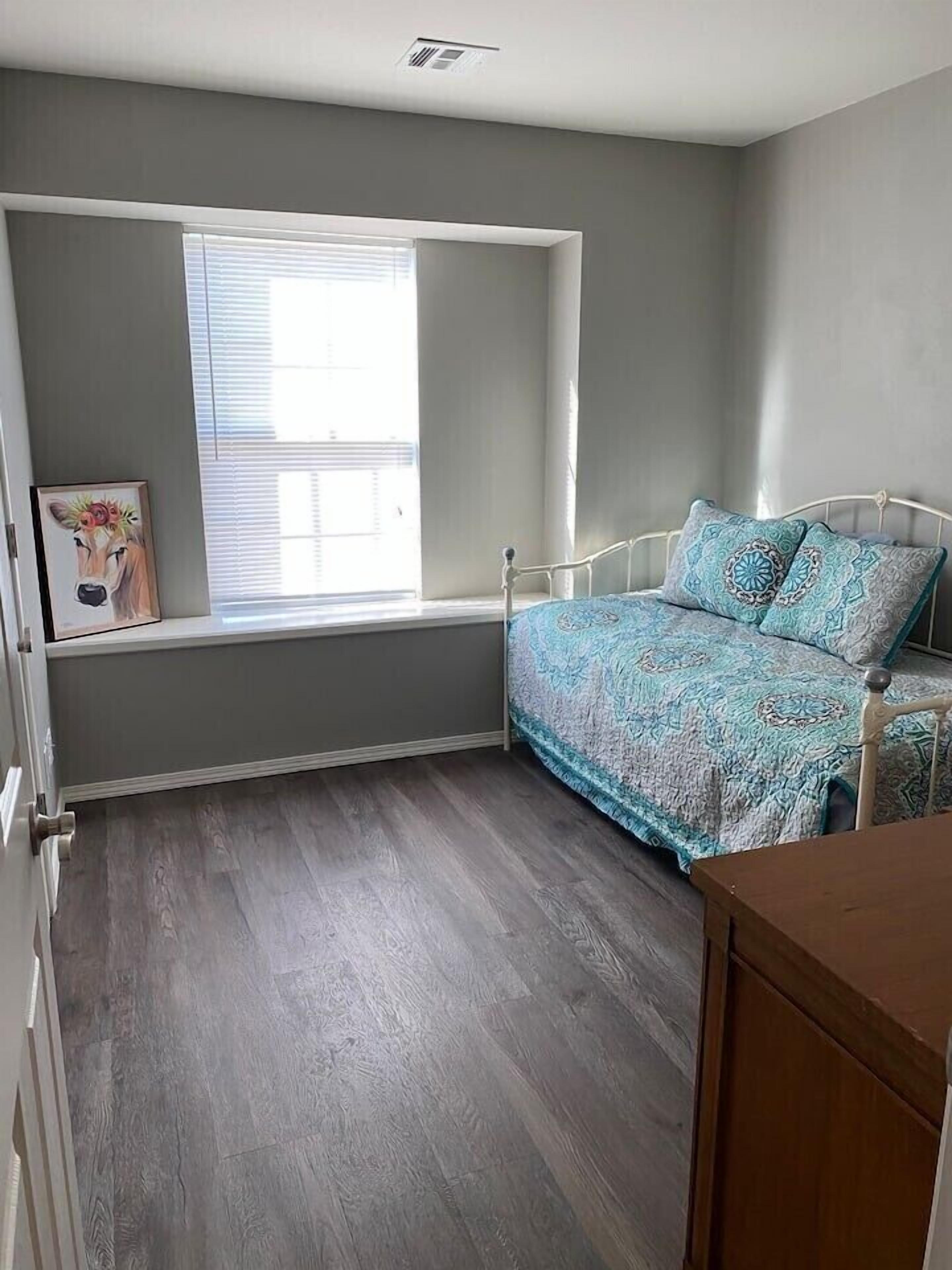 A bedroom with a built-in window seat, a bed with patterned bedding, and a wooden dresser.