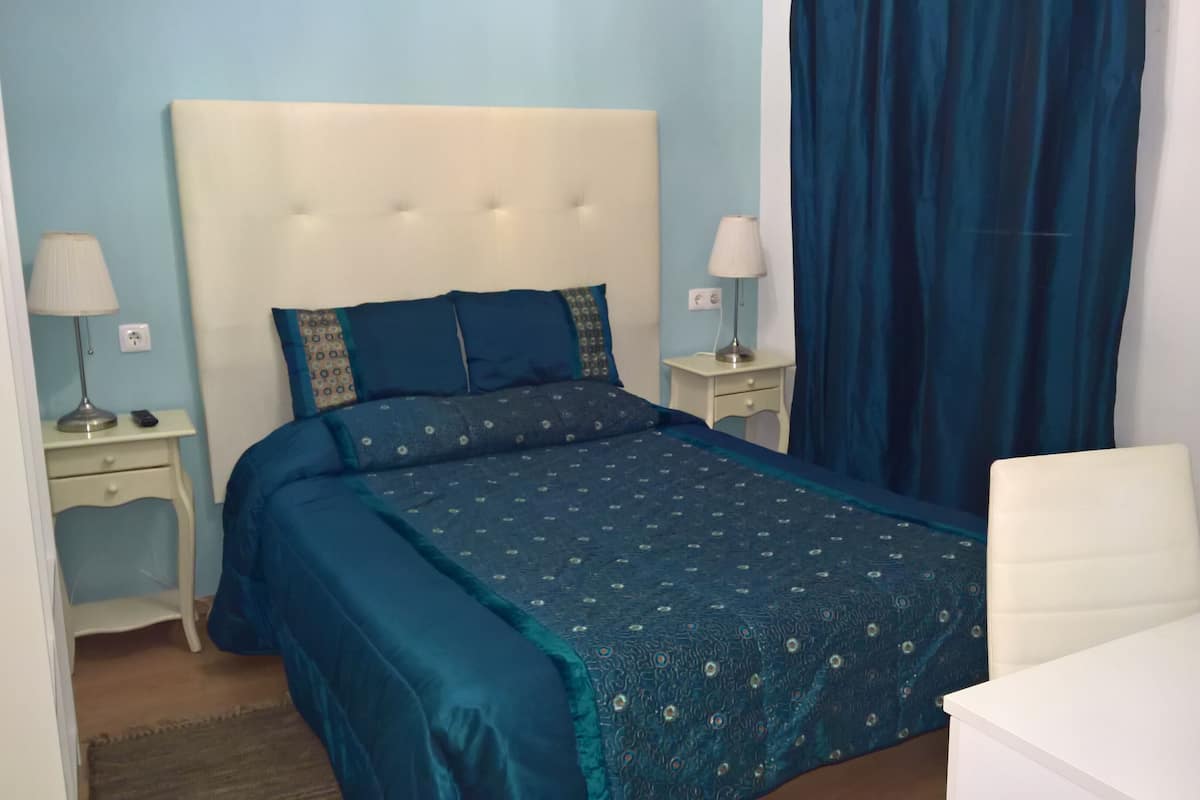 A bedroom with a bed, two bedside tables, a chair, and a window with curtains.