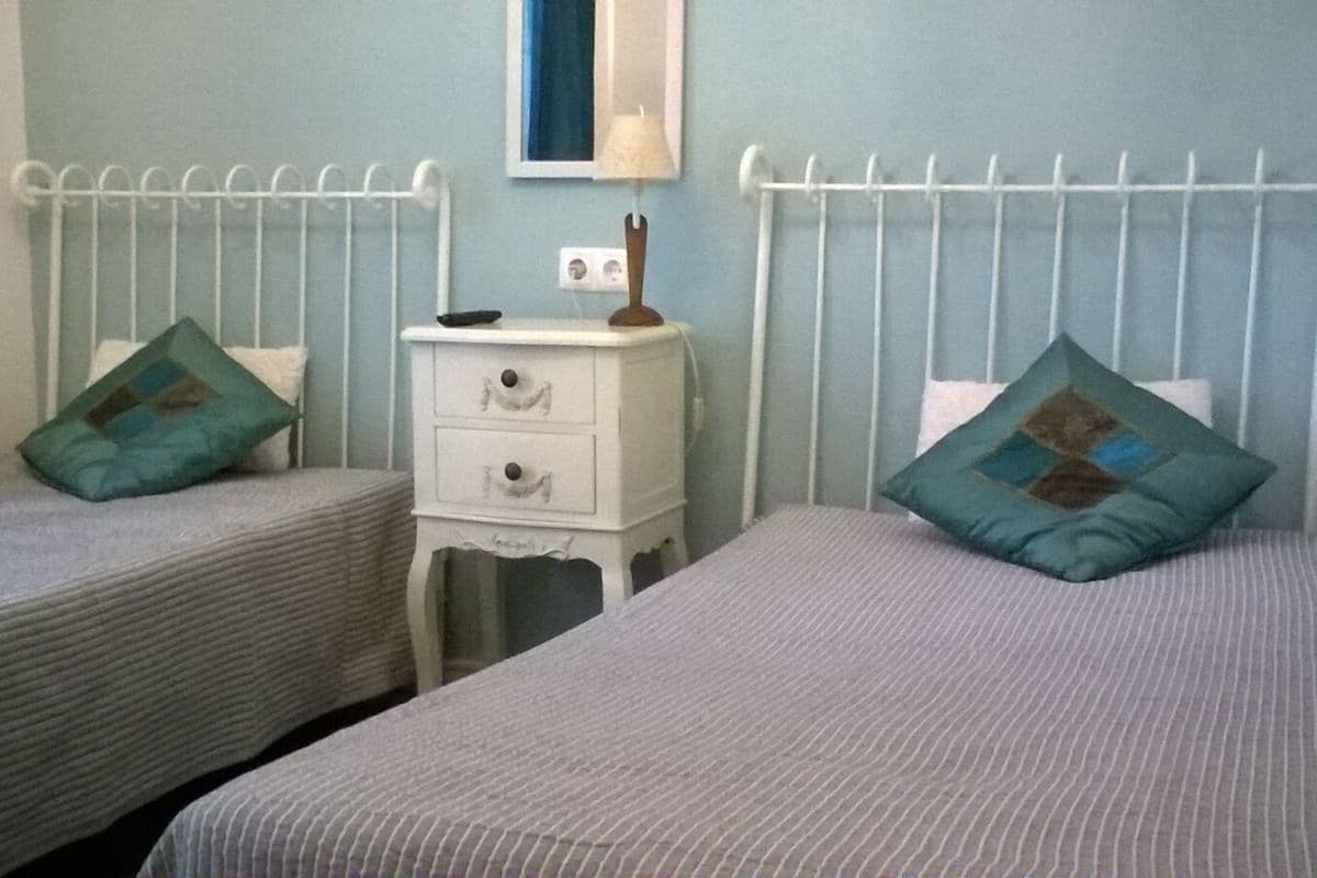 A bedroom with two single beds, a nightstand, and a wall-mounted shelf.