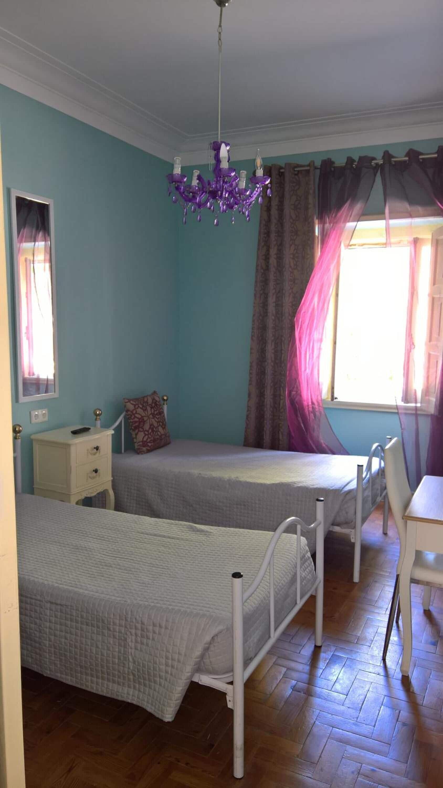 Ein Schlafzimmer mit zwei Betten, einem Schreibtisch, einem Stuhl, einer Kommode und einer Kristallleuchter.