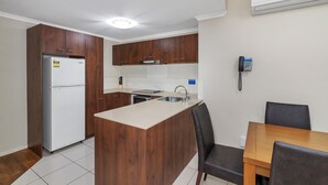 Une cuisine compacte avec des meubles en bois, un réfrigérateur blanc, un îlot central intégré et un coin repas avec une table et des chaises.