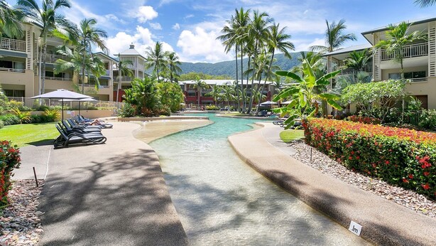 Un complexe hôtelier doté d’une piscine, de chaises longues, de palmiers et offrant une vue sur un paysage montagneux.
