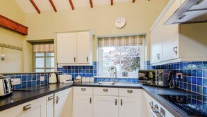 Une cuisine avec des meubles blancs, un plan de travail noir, une fenêtre donnant sur un beau paysage et une horloge au mur.