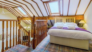 Une chambre avec un grand lit, des poutres en bois, un lustre et une moquette à carreaux.