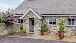 Une maison en pierre avec un toit en pente, un petit porche et deux plantes en pot.