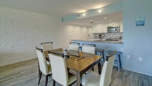 A dining area with a brick wall, a wooden table, and white chairs. - A Salty Day Getaway| Beach Boardwalk | Large Pool! (Port Aransas)