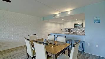 Uma sala de jantar com parede de tijolos, mesa de madeira e cadeiras brancas.