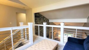 Un appartement de style « loft » avec un escalier, un banc rembourré et un canapé bleu.