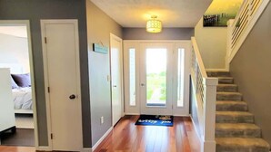 Un couloir avec un plancher en bois, un escalier et une porte donnant sur une pièce.