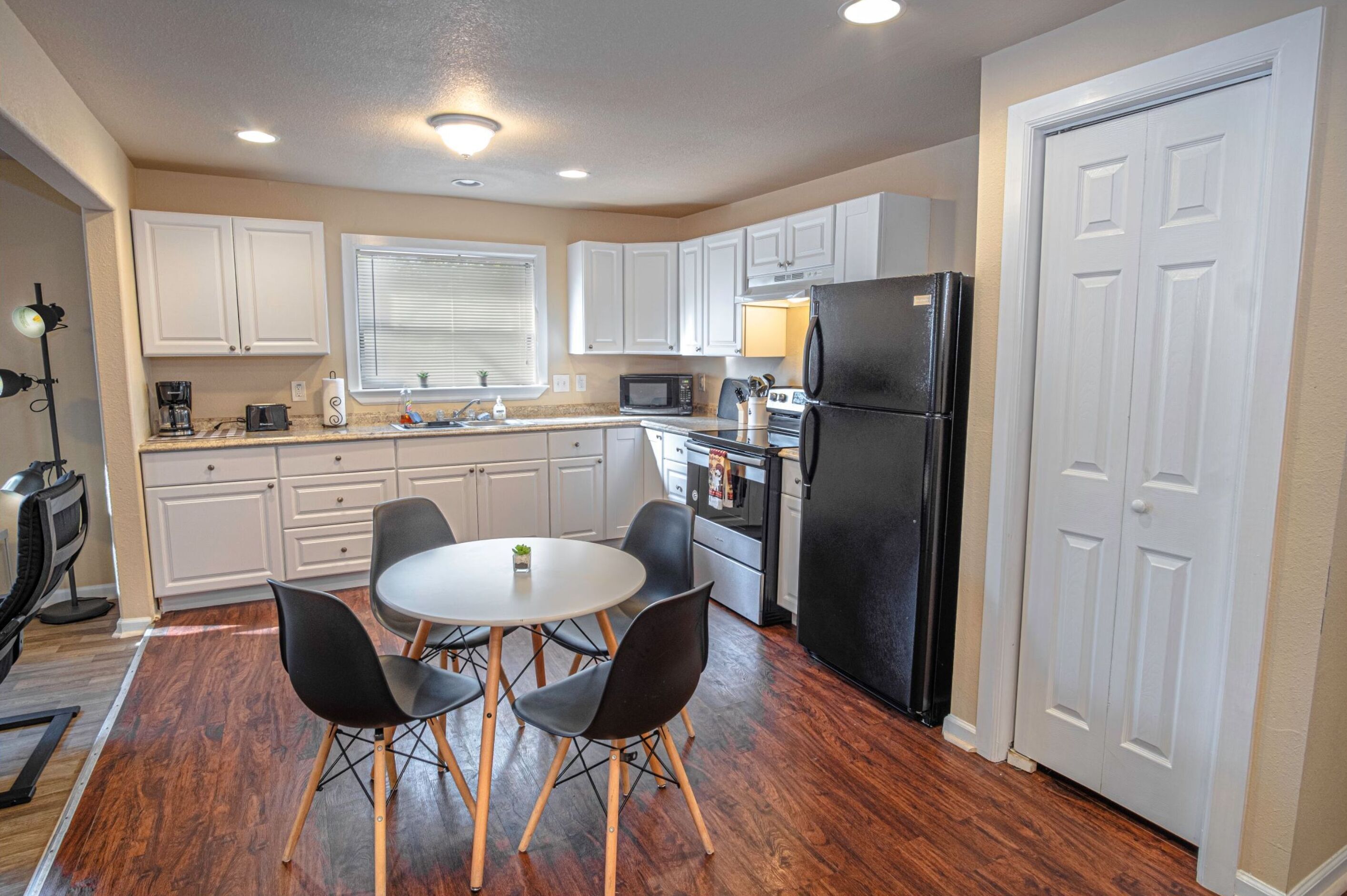 A modern kitchen with white cabinets, a black refrigerator, a microwave, and a dining area with a round table and four chairs.