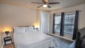 Ein Schlafzimmer mit Bett, Nachttischlampen, Deckenventilator, Tür und einem fensterbepflanzten Fenster.