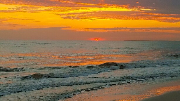 Un coucher de soleil sur l’océan, avec des vagues qui se rapprochent du rivage.