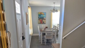 Un couloir mène à une salle à manger où se trouvent une table et des chaises, un tapis à motifs marins et un escalier doté d’une main courante.