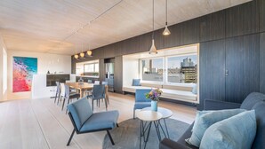 Ein modernes Wohnzimmer mit einer Couch, Sesseln, einem Esstisch und einem großen Fenster mit Blick auf die Stadt.