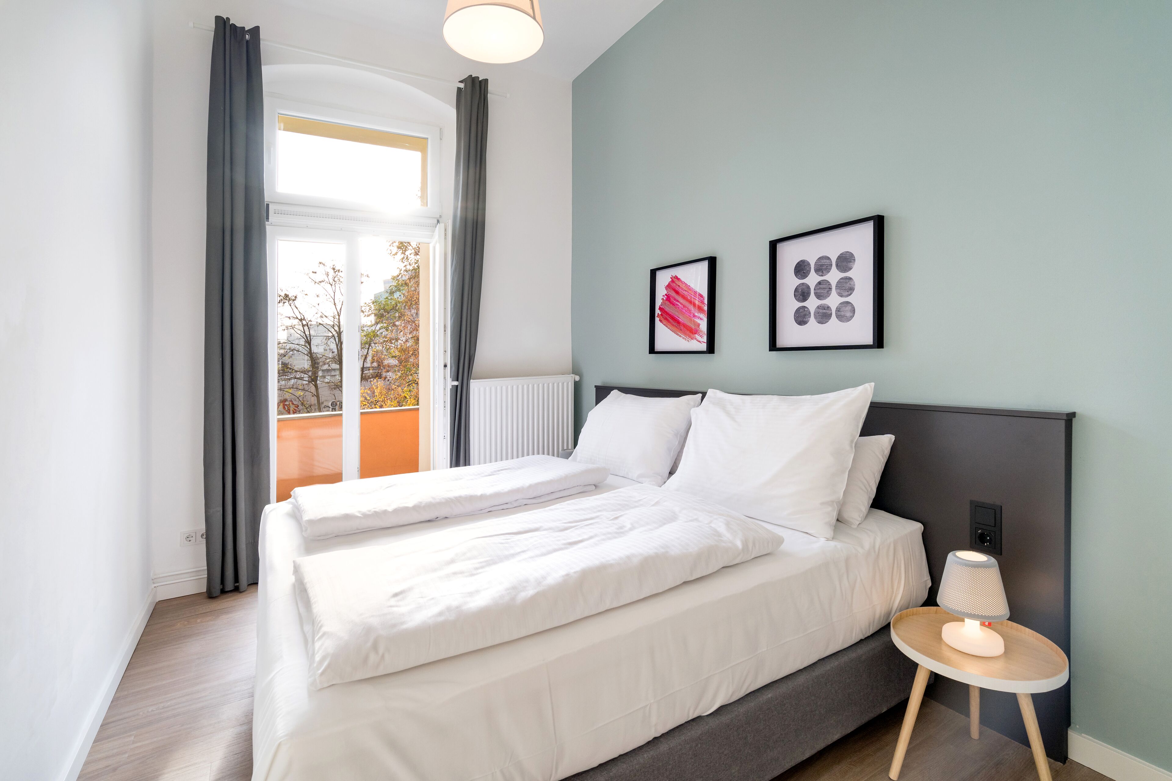 Ein modernes Schlafzimmer mit einem großen Bett, einem Nachttisch mit Lampe und zwei gerahmten Kunstwerken an der Wand.