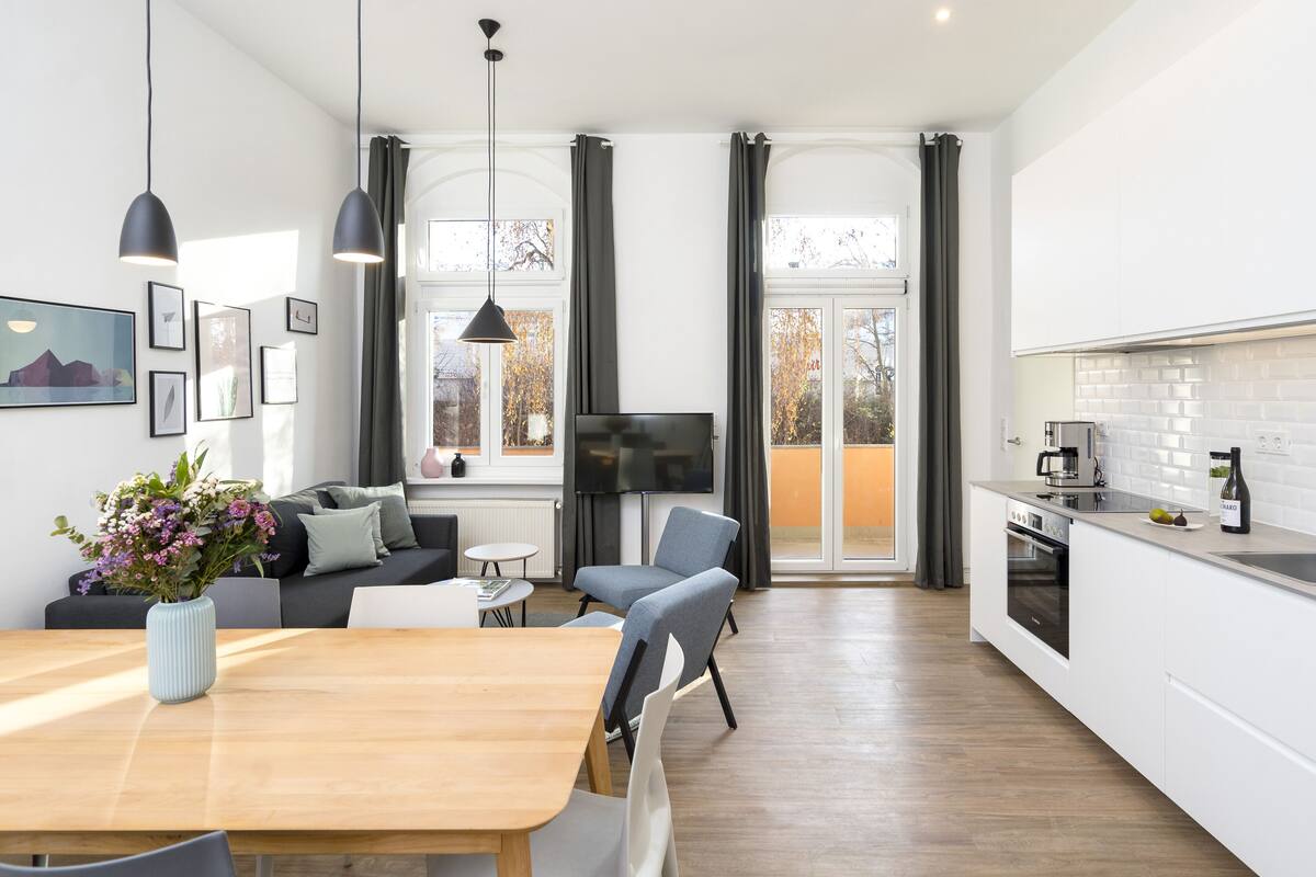 A modern kitchen with a dining area, a TV, and a large window with curtains.