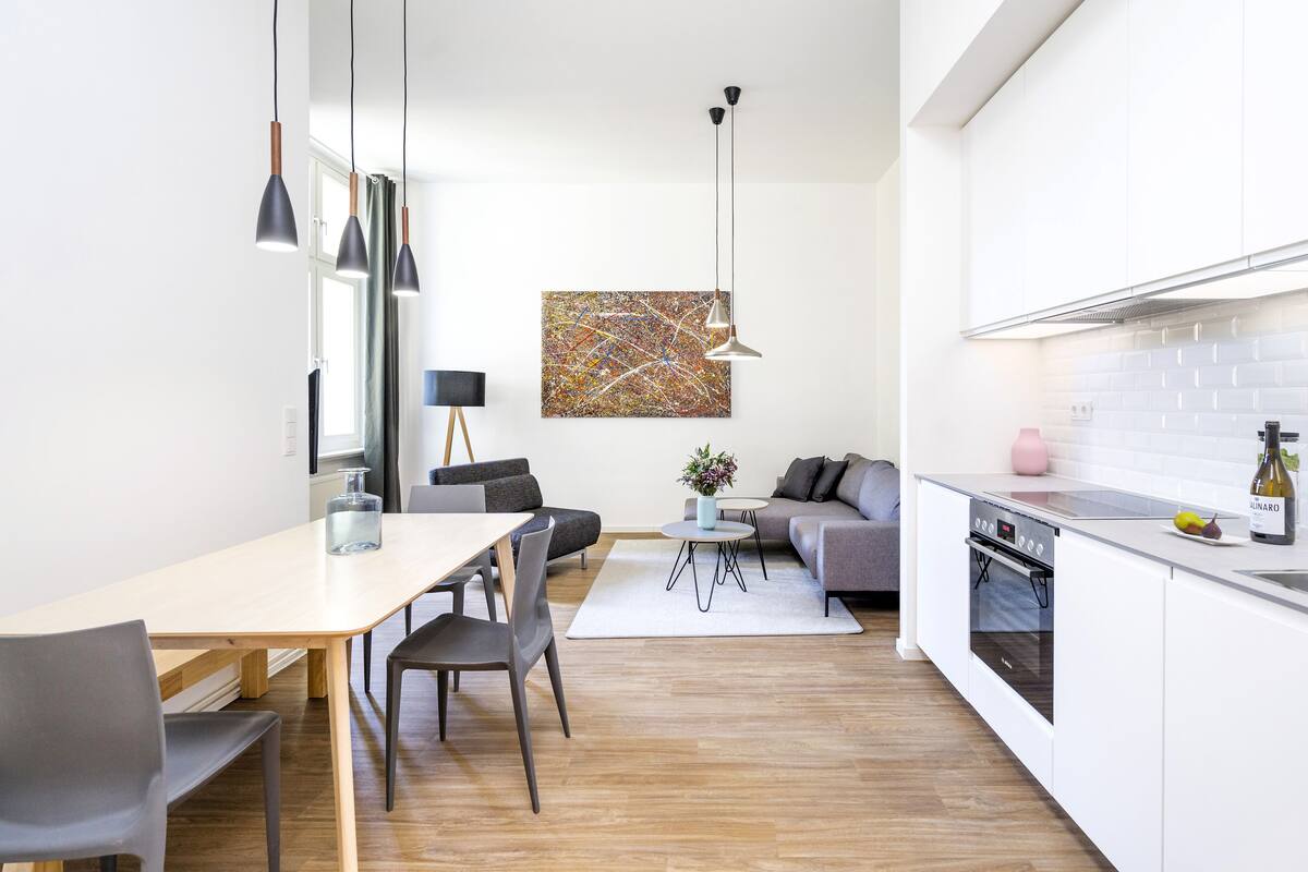 A modern kitchen with white cabinets, a built-in oven, and a dining area with a table and chairs.