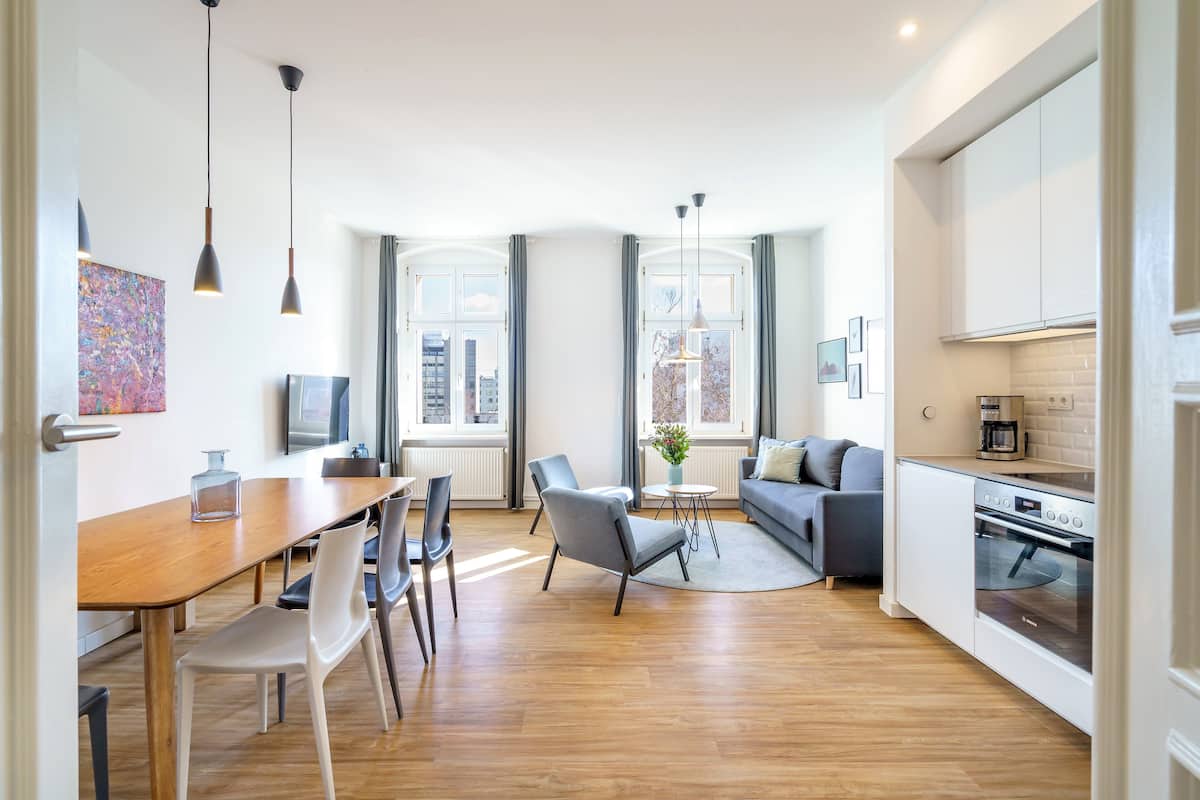 A modern kitchen with white cabinets, a built-in oven, and a dining area with a wooden table and chairs.