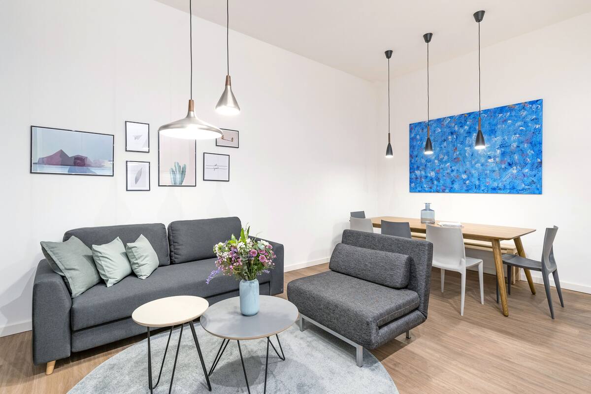 A modern living room with a grey sofa, a round coffee table, and a dining area with a wooden table and chairs.