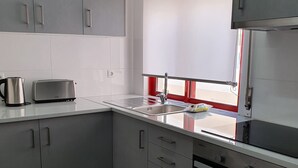 Una cucina moderna con mobili grigi, un lavello in acciaio inossidabile e una finestra con cornice rossa.