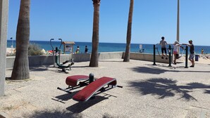 Un parco sulla spiaggia con attrezzature per l'esercizio fisico, palme e vista sull'oceano.