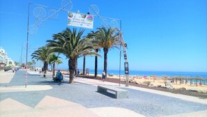 Una passeggiata lungomare con palme, un cartello con la scritta 'FESTAS DOS SANTOS POPULARES' e una vista aperta sul mare.