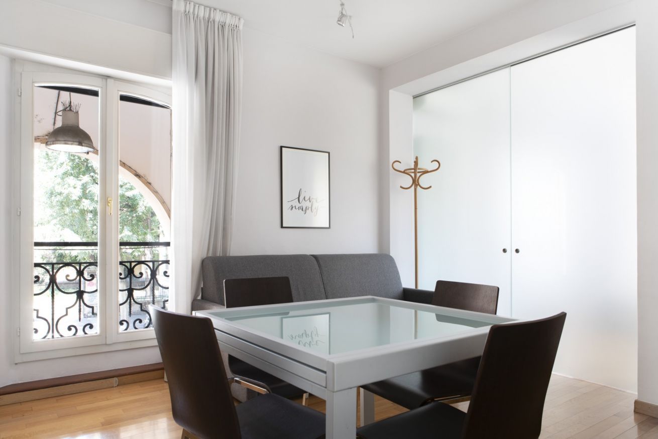 Una sala de estar moderna con una mesa de vidrio, un sofá gris y sillas negras.