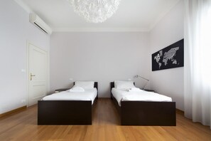A modern hotel room with two single beds, a large chandelier, a world map artwork, and a white door. - UR-NEST Marconi 3B (Bologna)