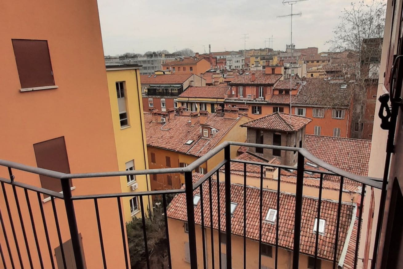 A view from a balcony overlooking a densely packed urban area with terracotta-tiled rooftops and a variety of building colors.