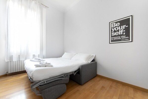 A modern bedroom with a bed, a grey sofa, and a motivational quote on the wall.