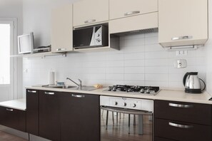 A modern kitchen with dark cabinets, a built-in microwave, a gas stove, and a kettle.