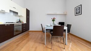 A modern kitchen with dark cabinets, a white countertop, and a dining area with a table and chairs.