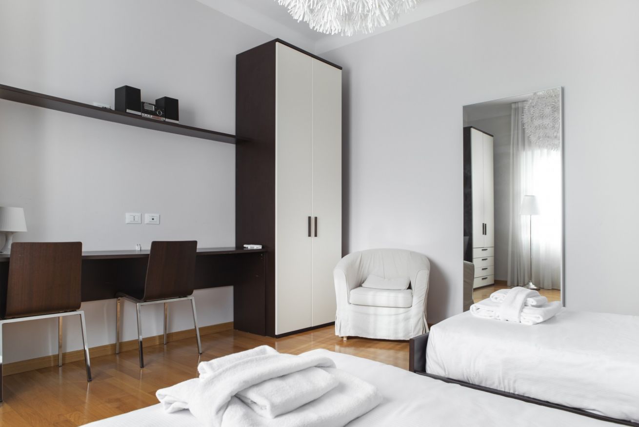 Una habitación de hotel moderna con escritorio, dos sillas, armario, cama y un espejo grande.