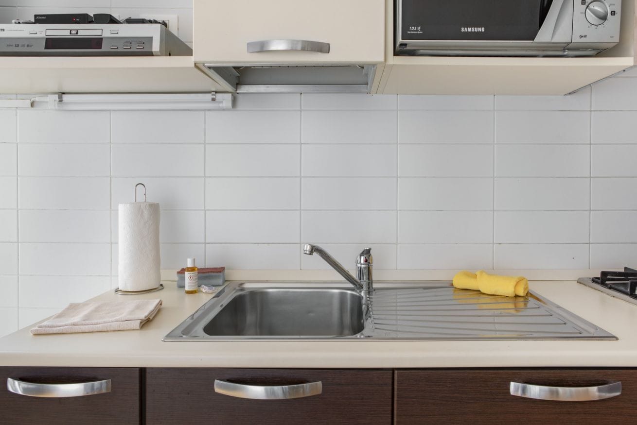 A kitchen with a stainless steel sink, a microwave, and a cabinet above the sink.