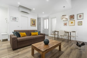 A modern living room with a brown sofa, wooden coffee table, and a dining area with a white table and chairs.