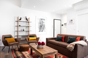 A modern living room with a brown leather sofa, two armchairs, a wooden coffee table, and a patterned rug.