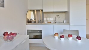 Une cuisine moderne avec des meubles blancs, des appareils en acier inoxydable et une table de salle à manger ronde ornée de pommes.
