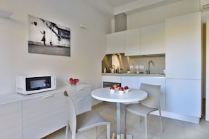 A modern kitchen with white cabinetry, a microwave, and a dining area with a white table and chairs.
