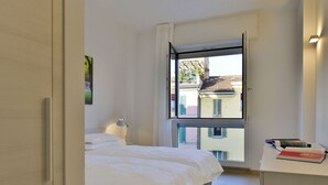 Une chambre avec deux lits, un bureau et une fenêtre donnant sur des immeubles.