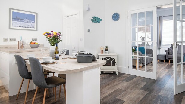 A modern kitchen with a central island, dining chairs, and a view of the living area through an open door.