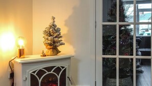 A cozy room with a white fireplace, a small Christmas tree, and a lit lamp.
