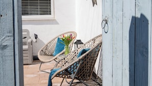 A patio with wicker chairs, a vase of flowers, and a window with blinds.