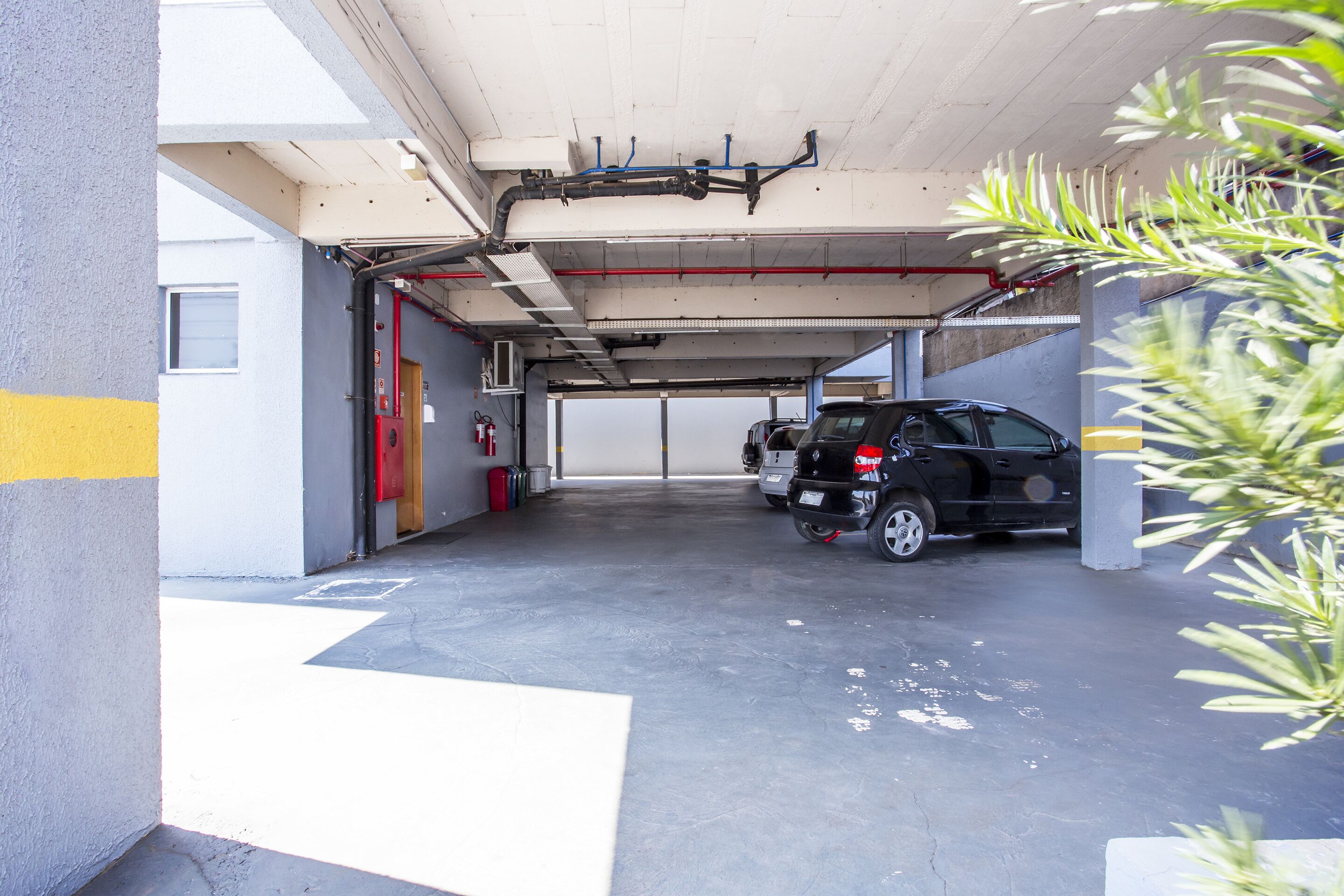 A parking garage with concrete floors and walls, a fire extinguisher, and a vehicle parked in the distance.