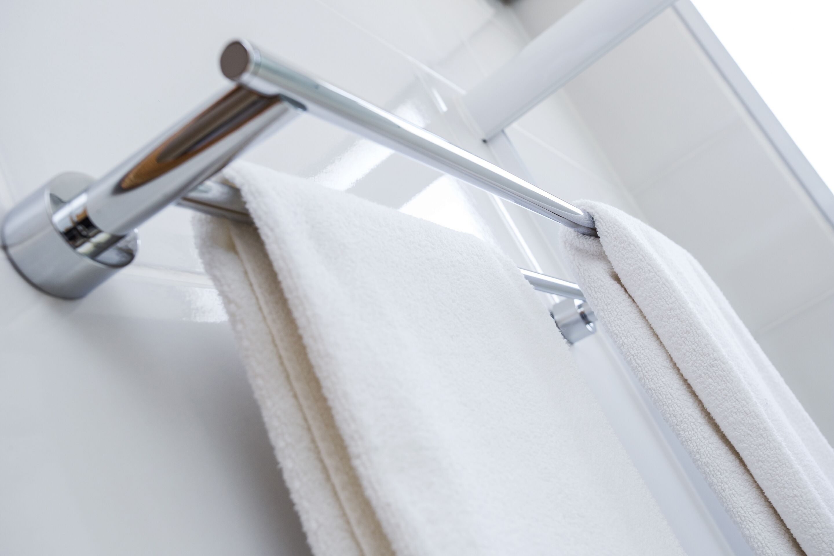 A white towel hanging on a chrome towel rack in a bathroom with white walls.