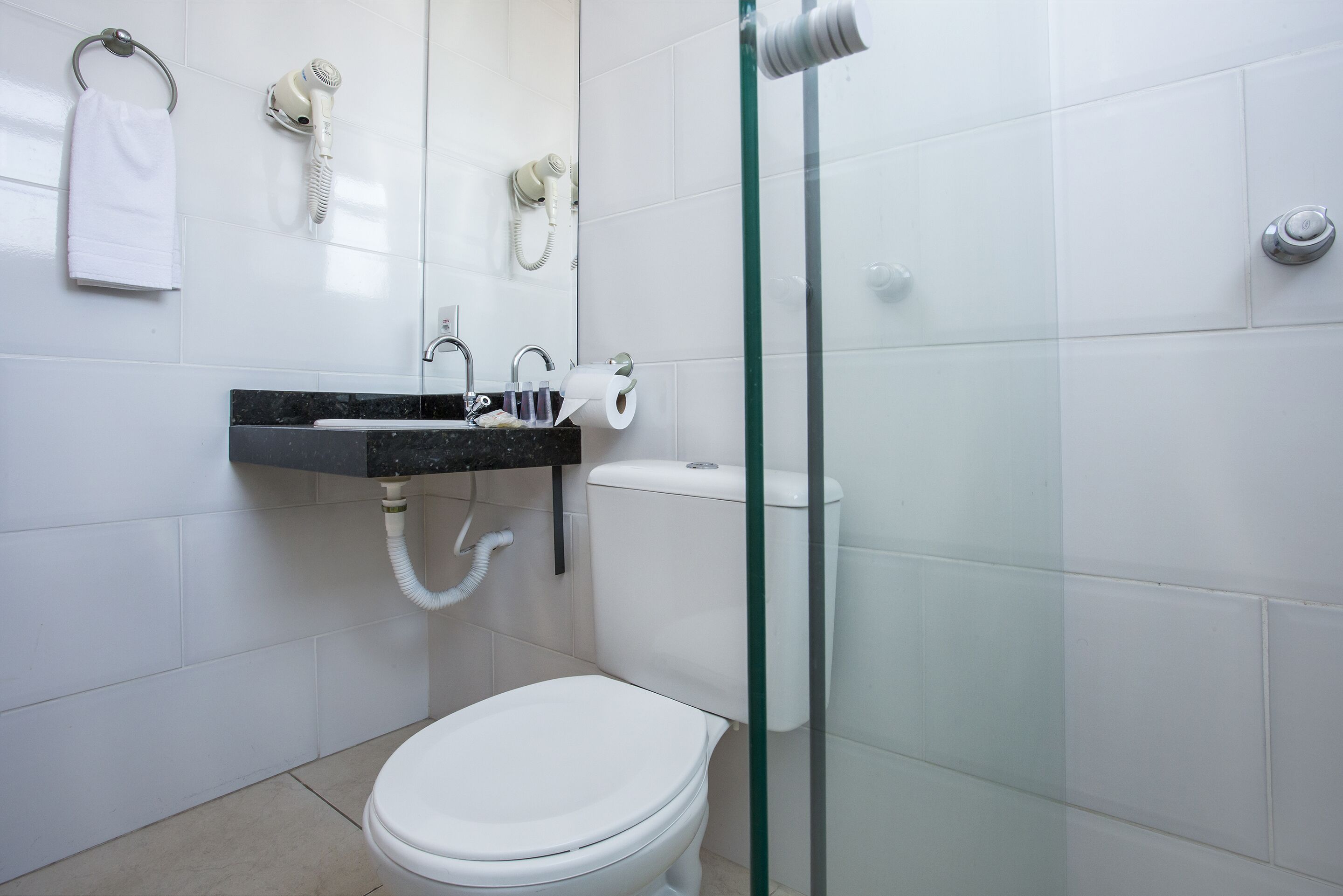 A bathroom with a white toilet, a glass-enclosed shower, a sink with a black countertop, and a towel hanging on a metal ring.