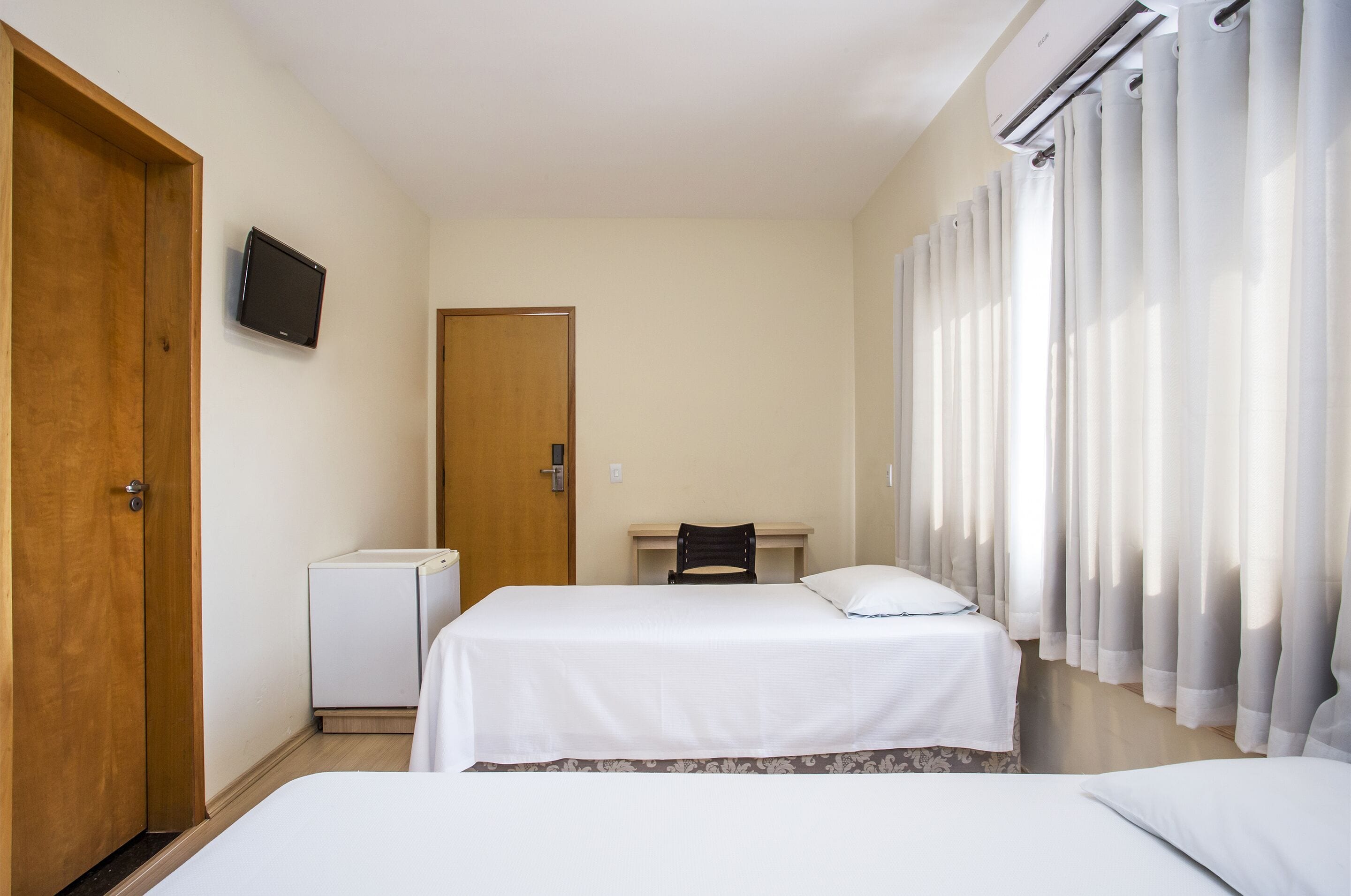 Hotellihuone, jossa on kaksi sänkyä, työpöytä, tuoli, televisio ja ilmastointilaite.