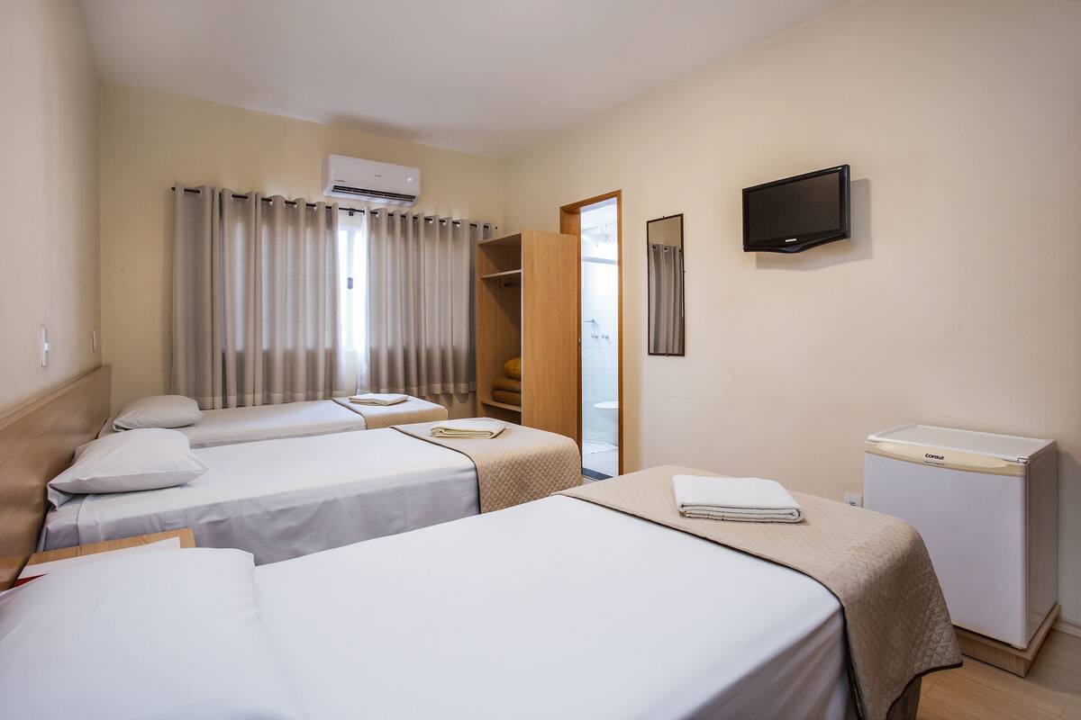 Ett hotellrum med två sängar, ett litet skrivbord med handfat, en tv och en luftkonditioneringsanläggning.