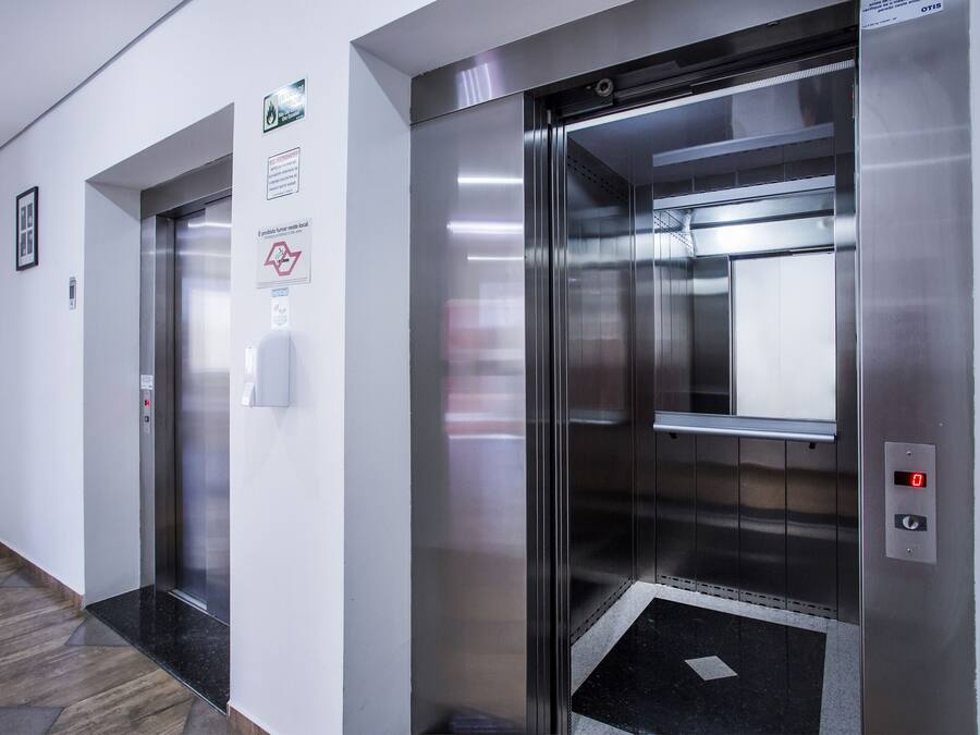 Two elevator doors in a hallway with a floor-to-ceiling mirror on one side and a wall-mounted sign with safety instructions.