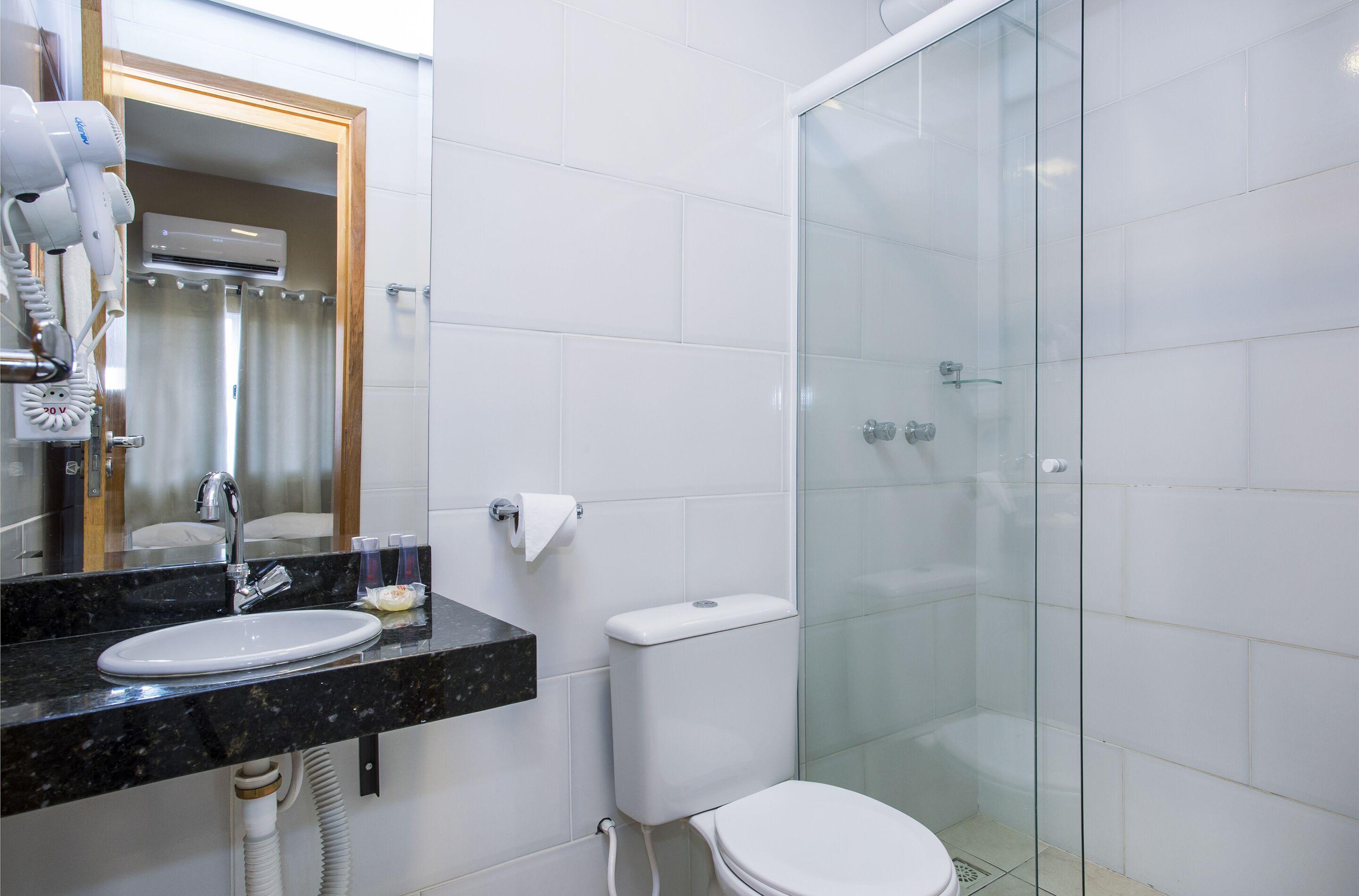 Un baño con ducha de vidrio, un lavamanos con encimera de mármol y un inodoro.